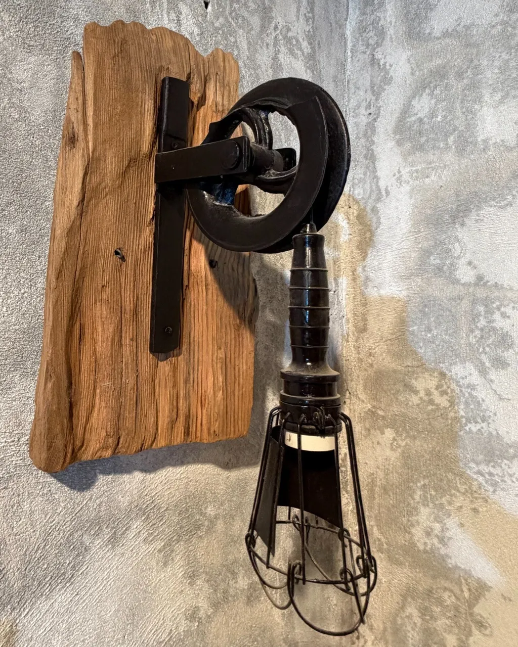Aplique de pared con una polea de hierro antigua sobre madera y una lámpara de jaula