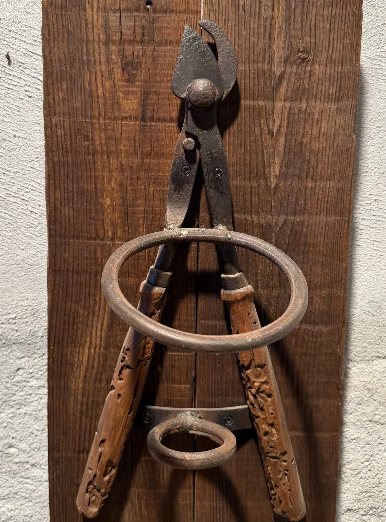 Botellero de pared hecho con unas tenazas antiguas y argollas de hierro sobre una tabla