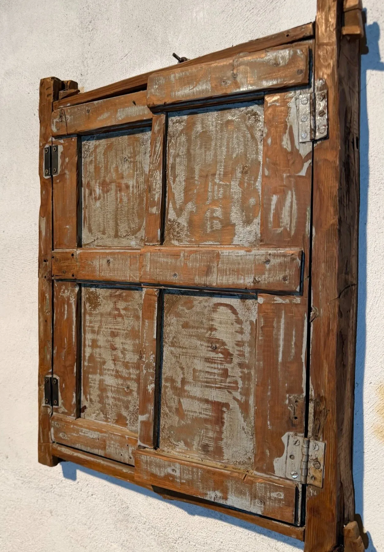 Contraventana antigua de madera con pintura desgastada y bisagras de hierro, colgada en la pared