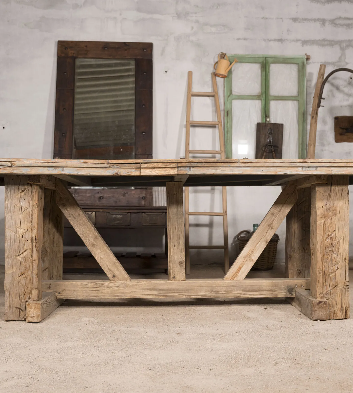 Mesa de comedor vista de frente en el taller, con escalera y ventana verde al fondo